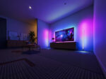 Lampadaire LED d’angle intelligent en forme de tube, sur pied, design minimaliste noir, lumière RGB personnalisable dans un salon moderne.