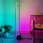 Lampadaire LED d’angle intelligent forme géométrique moderne Lampadaire LED d’angle intelligent forme géométrique moderne, à la structure noire minimaliste, doté d’une lumière RGB dans un coin de salon.