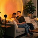 Lampe halo coucher de soleil LED avec télécommande Lampe halo coucher de soleil LED avec télécommande posée sur une table, projette un cercle lumineux chaud sur le mur, télécommande visible au premier plan.