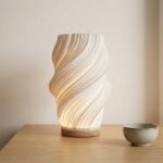 Lampe de table LED design contemporain La lampe de table LED design contemporain avec forme ondulée moderne, lumière douce diffusée créant une ambiance apaisante, objet déco élégant posé sur une table intérieur en bois minimaliste.