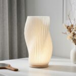 Lampe de table LED dimmable abat-jour plissé avec structure ondulée moderne diffusant lumière douce et réglable, posée sur table.