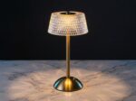 La lampe de table LED art déco rechargeable, abat-jour effet cristal et facettes diamant, pied brossé doré, posée sur un marbre clair.