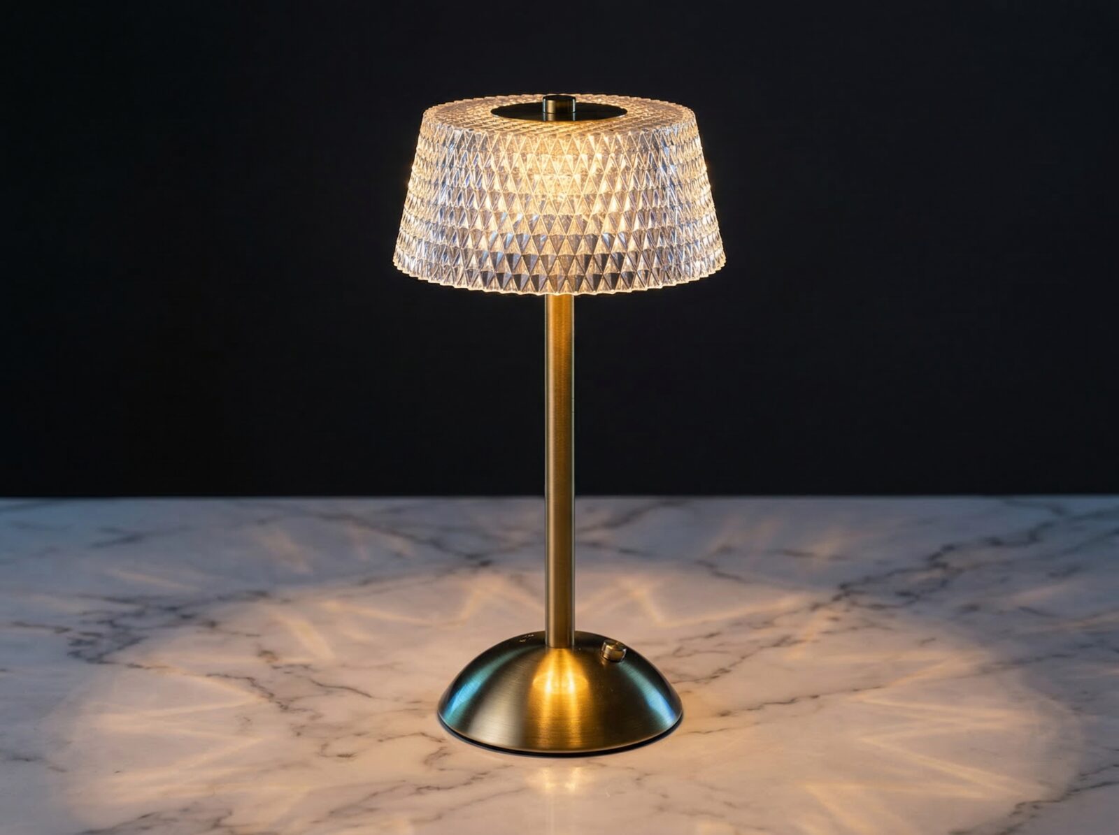 La lampe de table LED art déco rechargeable, abat-jour effet cristal et facettes diamant, pied brossé doré, posée sur un marbre clair.