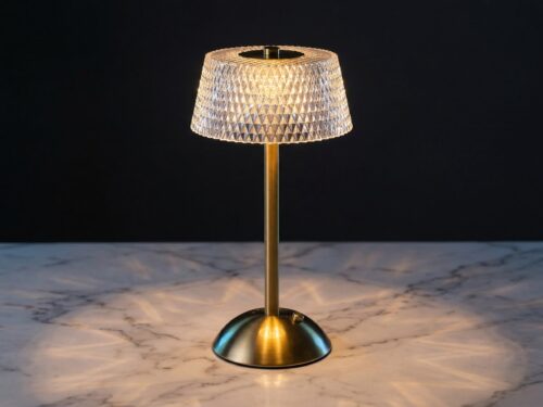 La lampe de table LED art déco rechargeable, abat-jour effet cristal et facettes diamant, pied brossé doré, posée sur un marbre clair.
