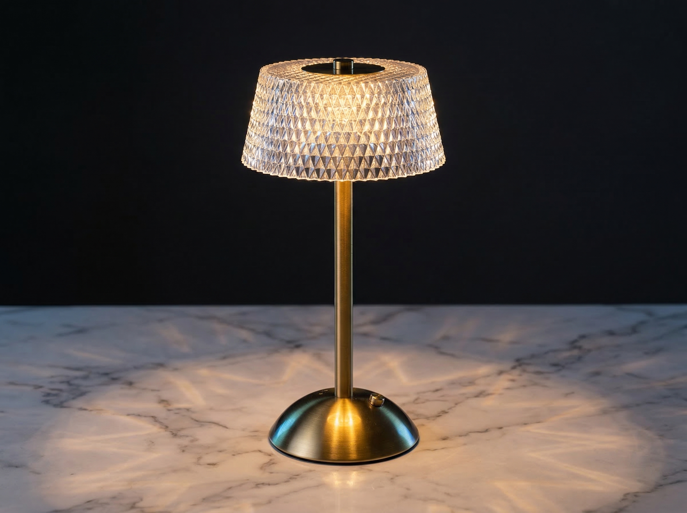 La lampe de table LED art déco rechargeable, abat-jour effet cristal et facettes diamant, pied brossé doré, posée sur un marbre clair.