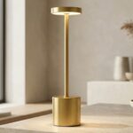 La lampe de table sans fil tactile et élégante en métal doré, avec une forme cylindrique moderne diffusant une lumière douce, posée sur une table, design minimaliste chic.